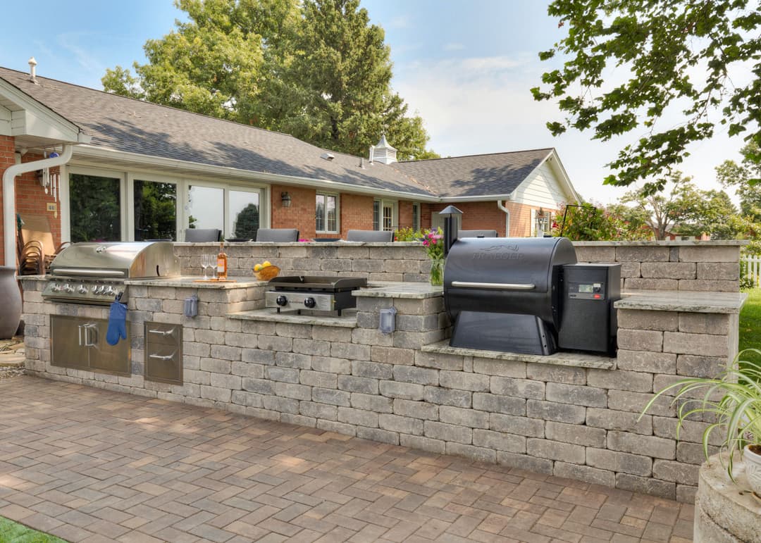 Modern outdoor kitchen with built-in grill and smoker, set in a landscaped backyard.