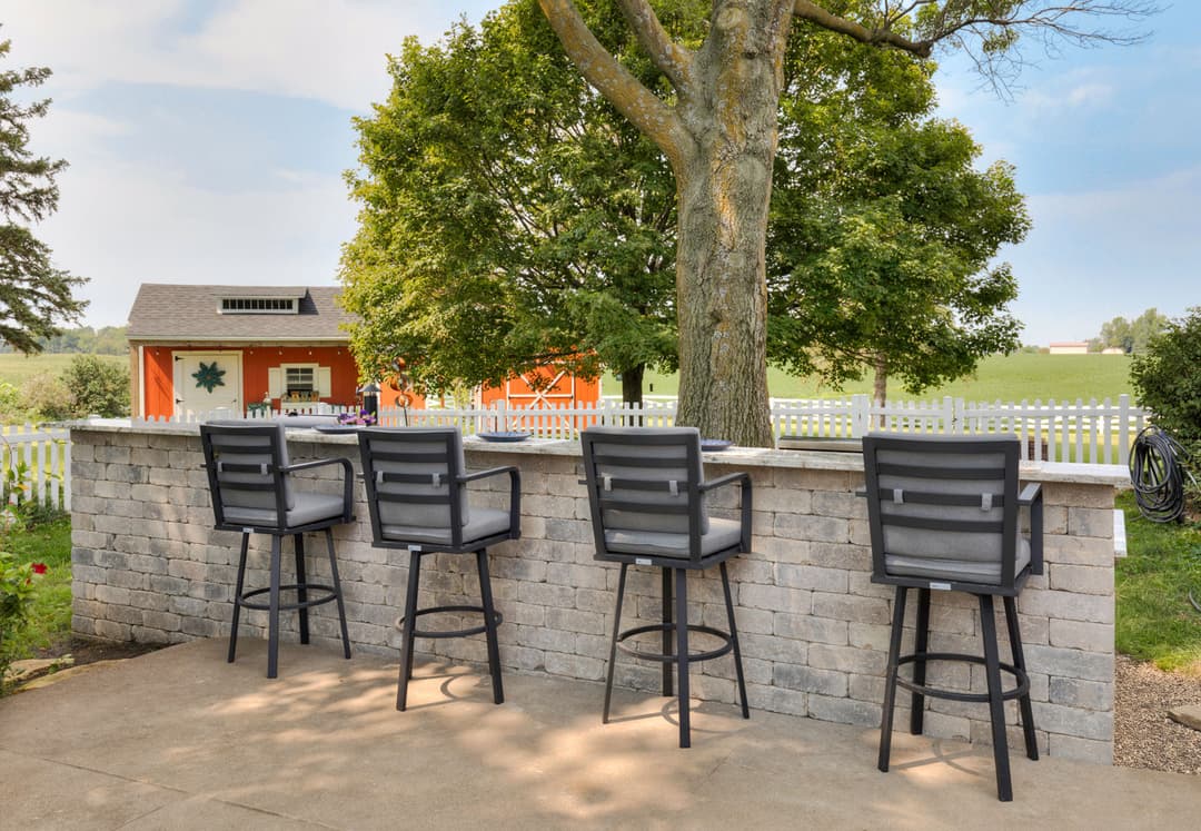 Outdoor bar seating with high stools, stone counter, and tree in a scenic backyard setting.