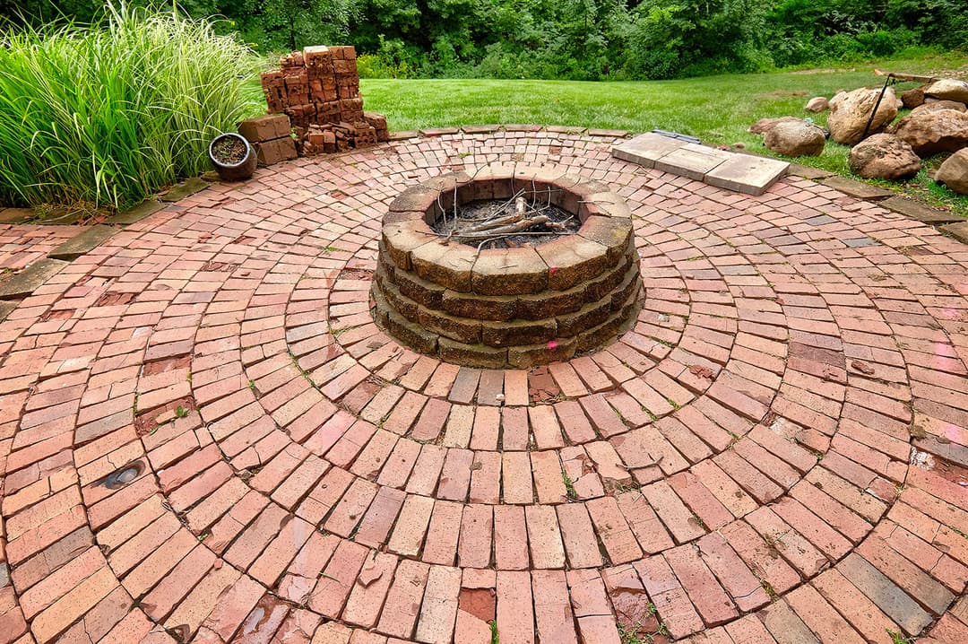 Circular brick fire pit surrounded by grass and landscaping, ideal for outdoor gatherings.