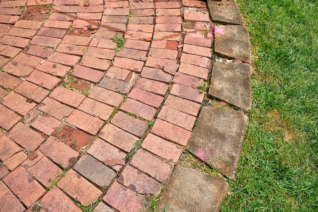 Curved brick pathway with grass and subtle pink markings on uneven stones.