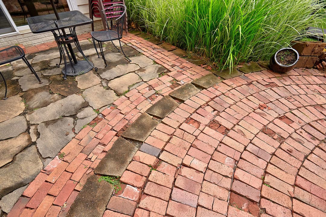 Outdoor patio featuring a circular brick pathway, stone tiles, and tall green grass.