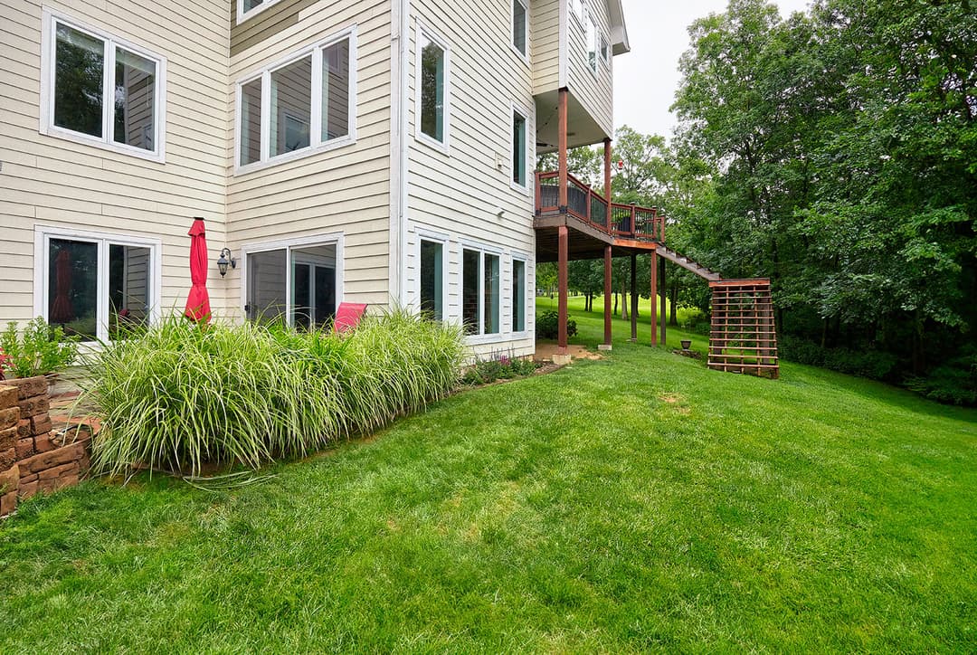 Modern two-story home exterior with landscaped lawn and garden, featuring large windows and deck.