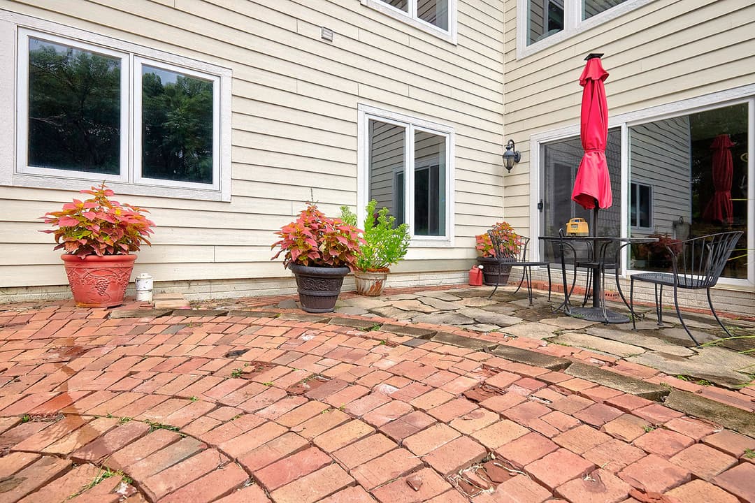 Cozy patio with brick flooring, potted plants, table, and umbrella near glass doors.