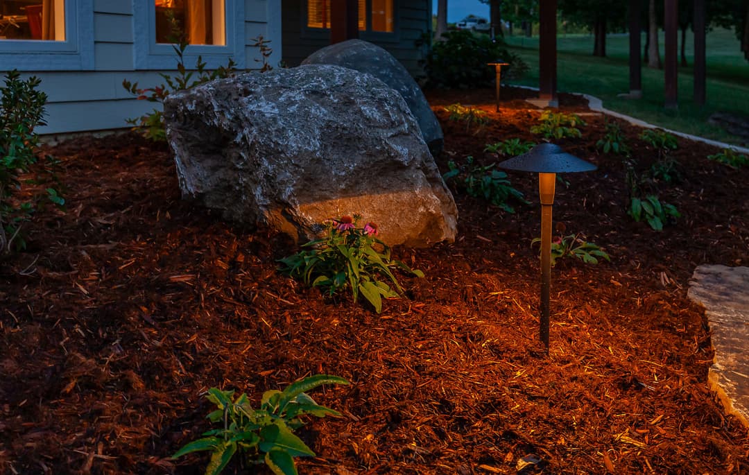 Well-lit garden scene featuring a large rock, flowers, and stylish landscape lighting.