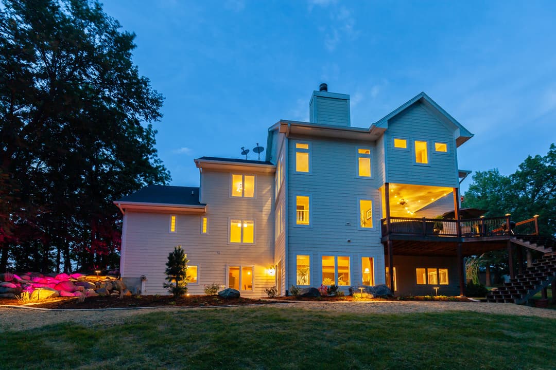 Elegant two-story house at dusk with illuminated windows and landscaped yard.