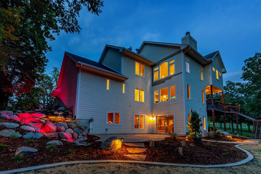 Modern two-story home exterior at dusk with illuminated windows and landscaped yard.