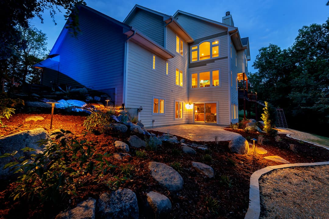 Modern home exterior illuminated at dusk, featuring landscaped garden and stone pathways.