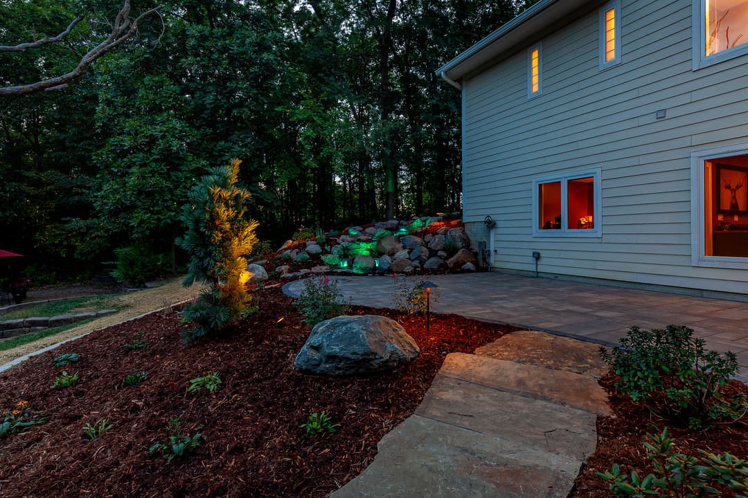 Elegant backyard with stone patio, landscaped garden, and ambient lighting at dusk.