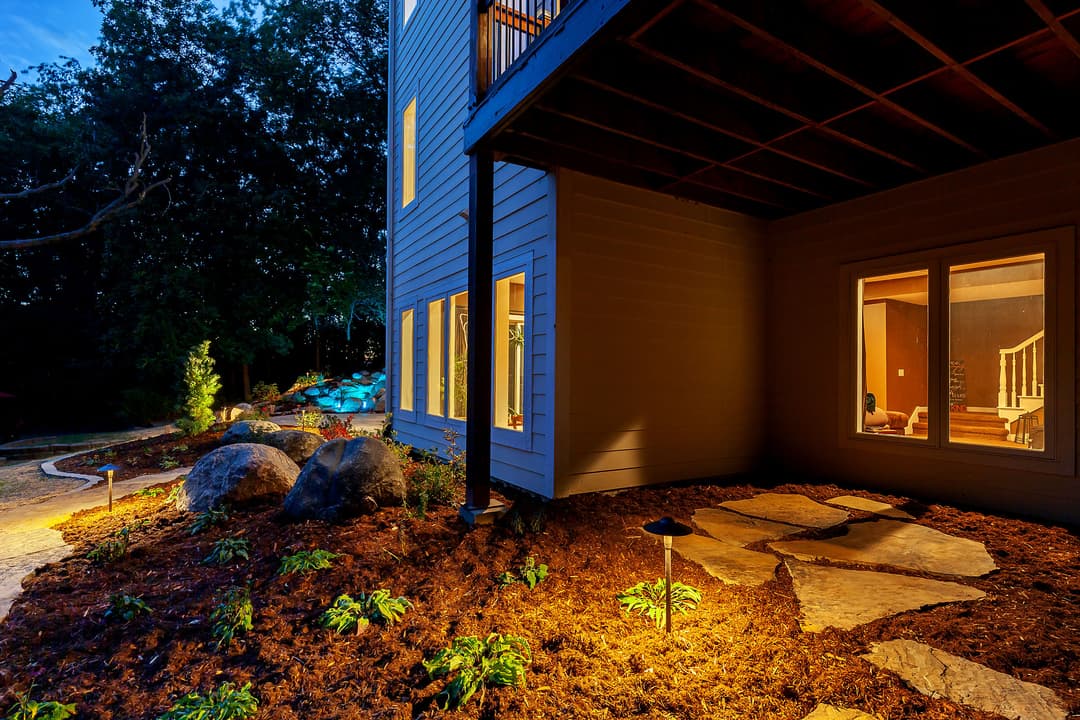 Modern home exterior with illuminated stone pathway and landscaped garden at dusk.