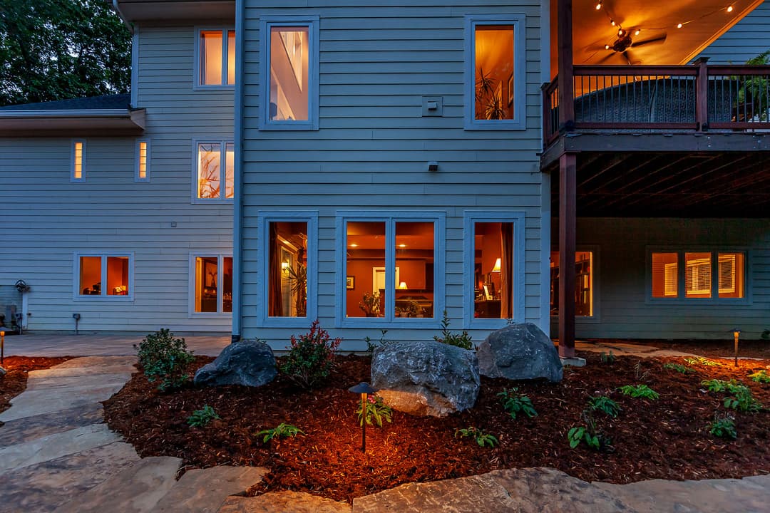 Modern two-story home with landscaped garden and outdoor lighting at dusk.