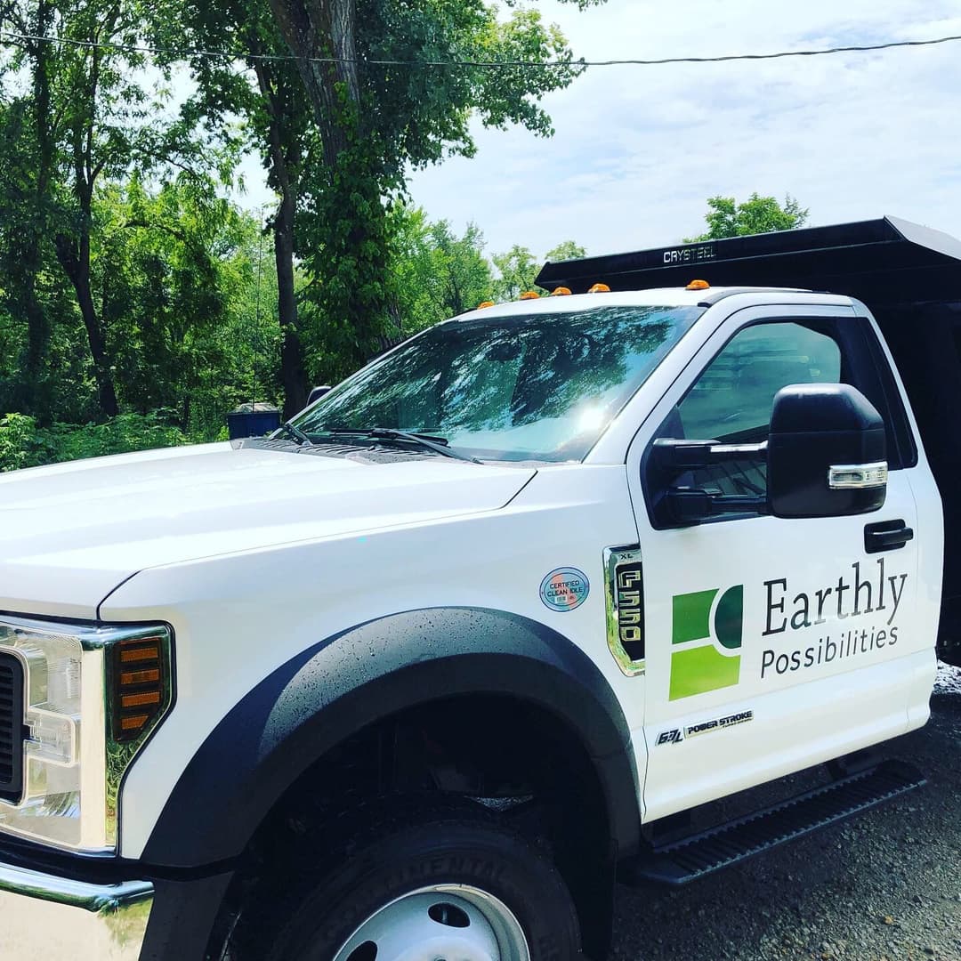 White pickup truck with Earthly Possibilities logo parked in a green, wooded area.