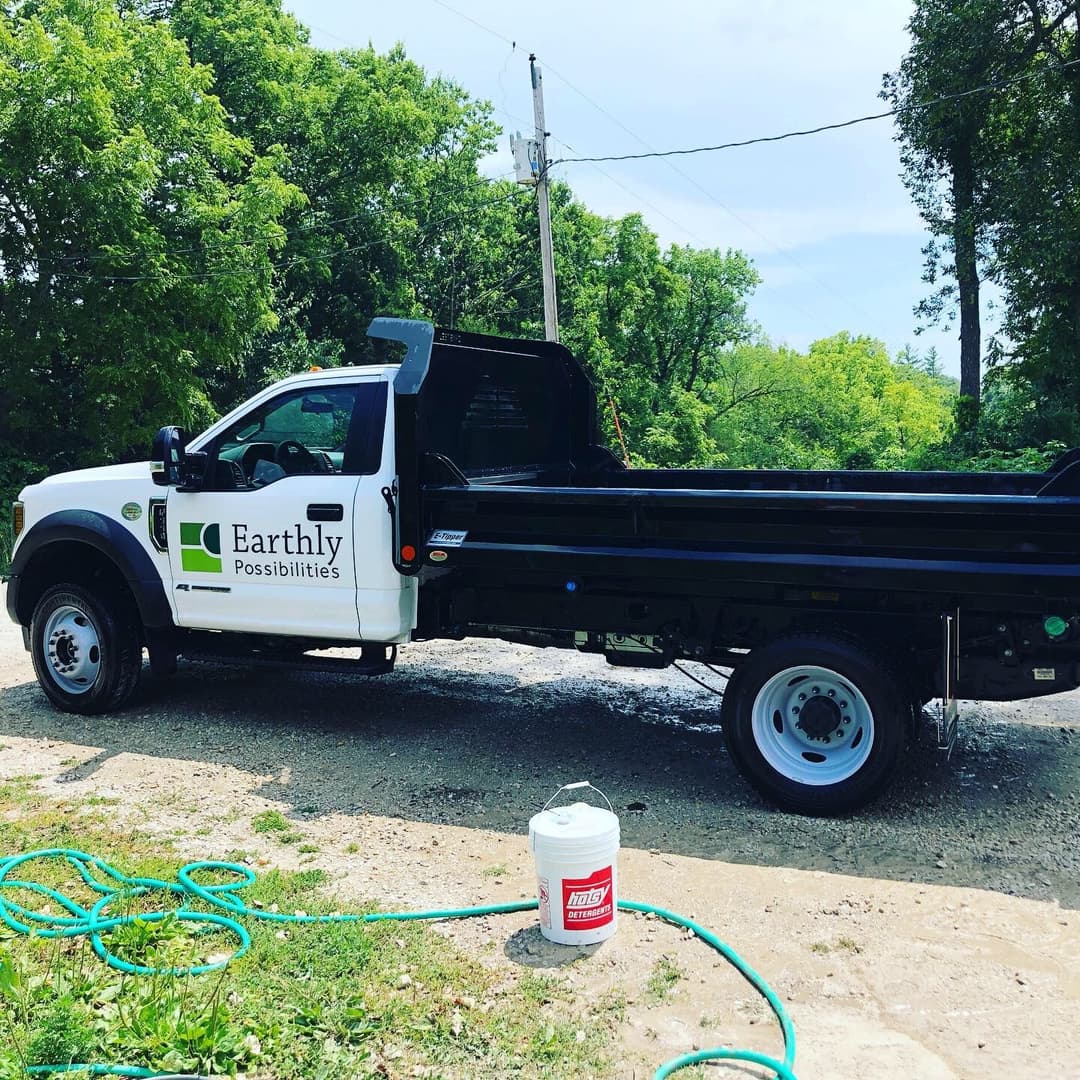Earthly Possibilities logo on a pickup truck parked in a green, wooded area.