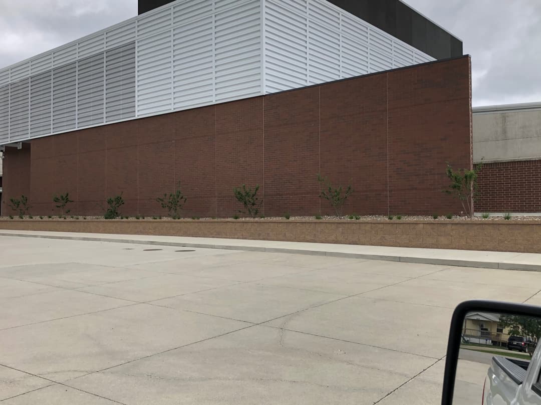 Modern building exterior with brick and metal panels, landscaped with small plants.