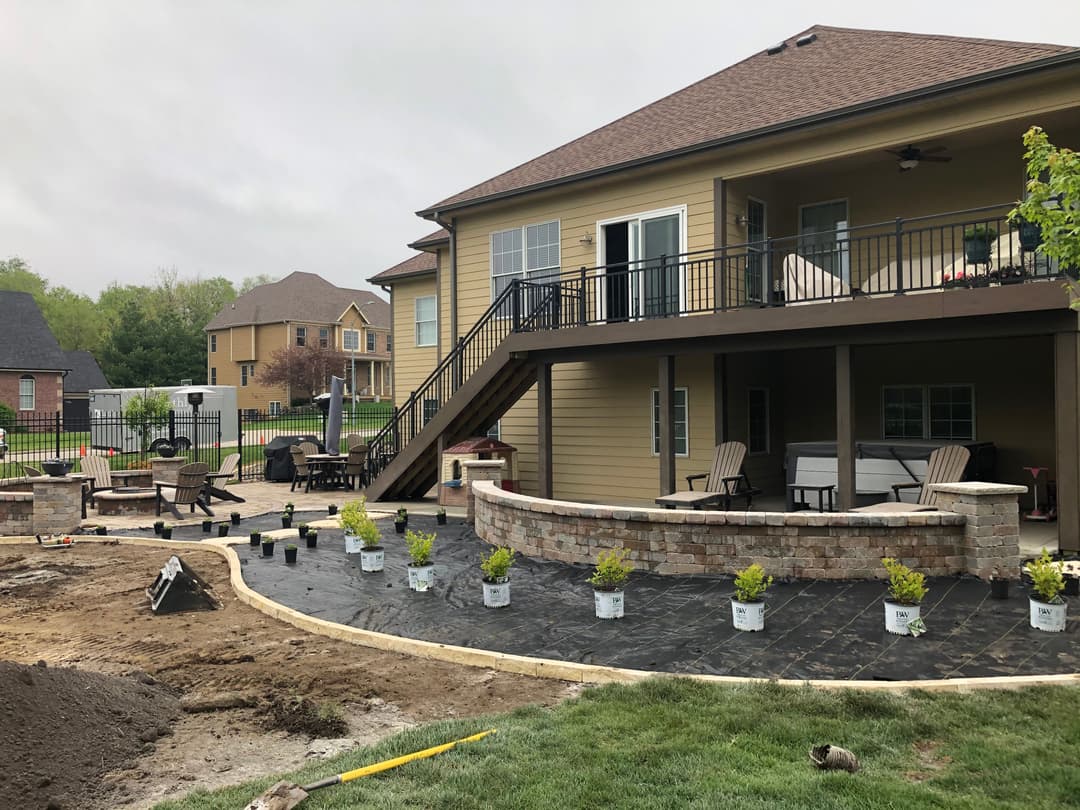Newly landscaped backyard patio with seating, plants, and a modern house in the background.