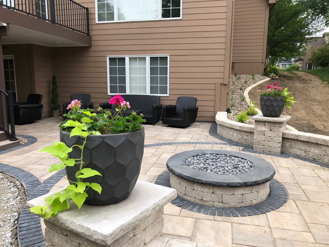 Contemporary outdoor patio with stone seating, flower pots, and a fire pit in a residential area.