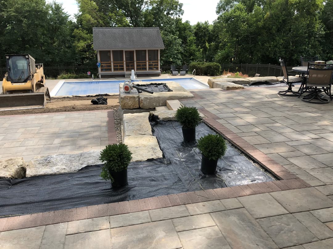 Landscape construction with a pool, patio stones, and plants in pots for outdoor renovation.