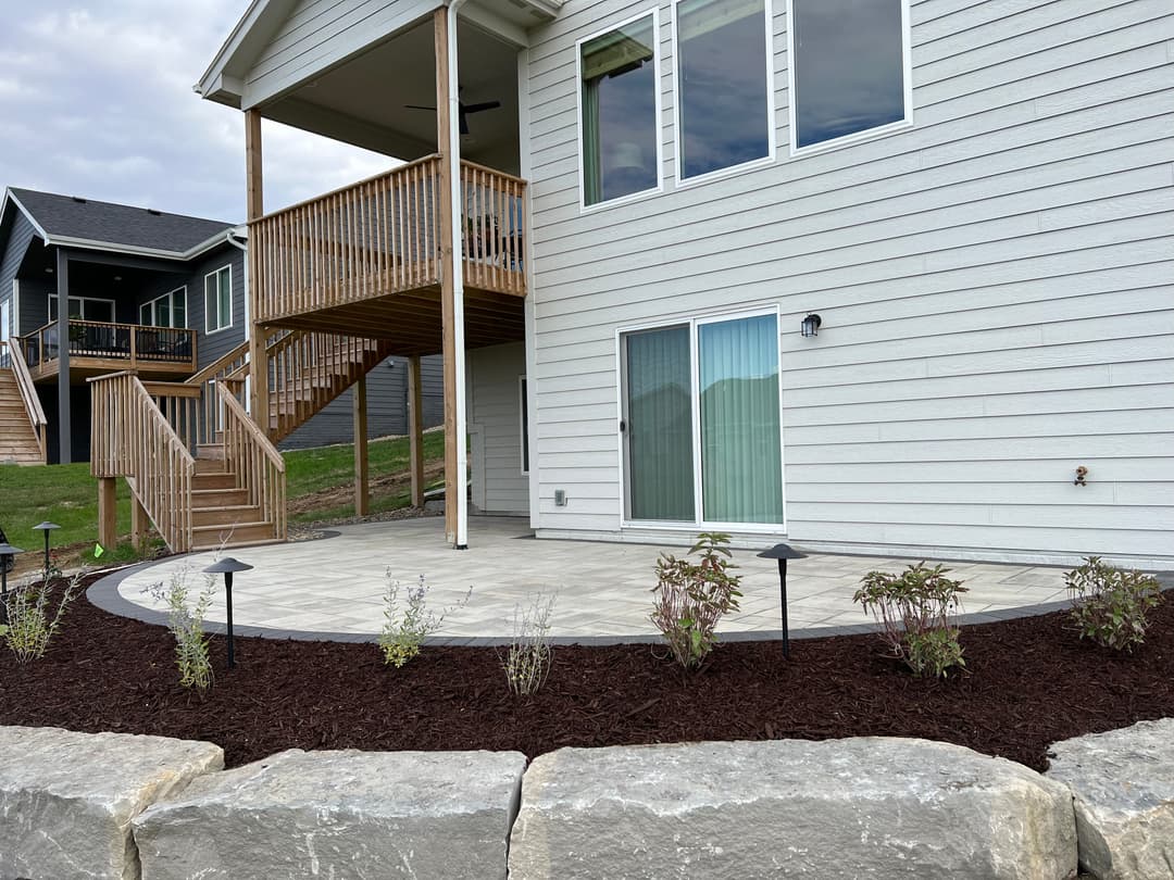 Modern home exterior with a landscaped patio, stone border, and outdoor lighting.