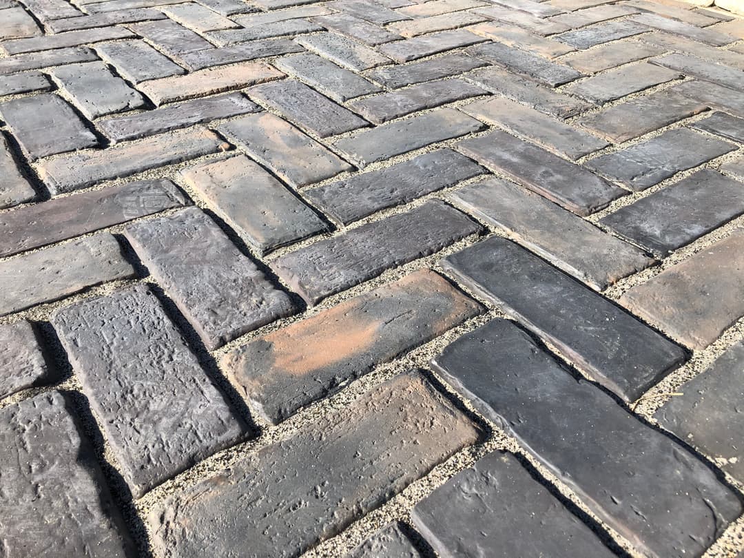 Herringbone pattern brick pavement in dark tones with textured surface detail.