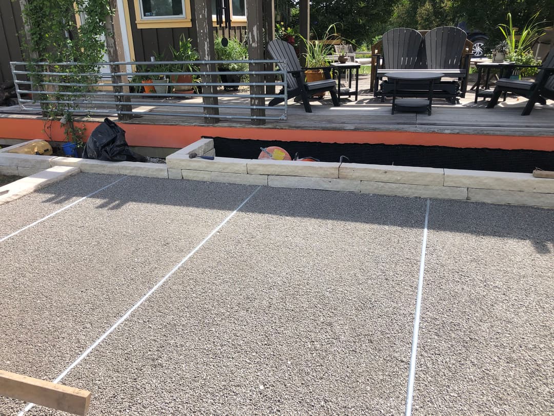 Construction site with gravel surface and marked lines, surrounded by planters and seating area.