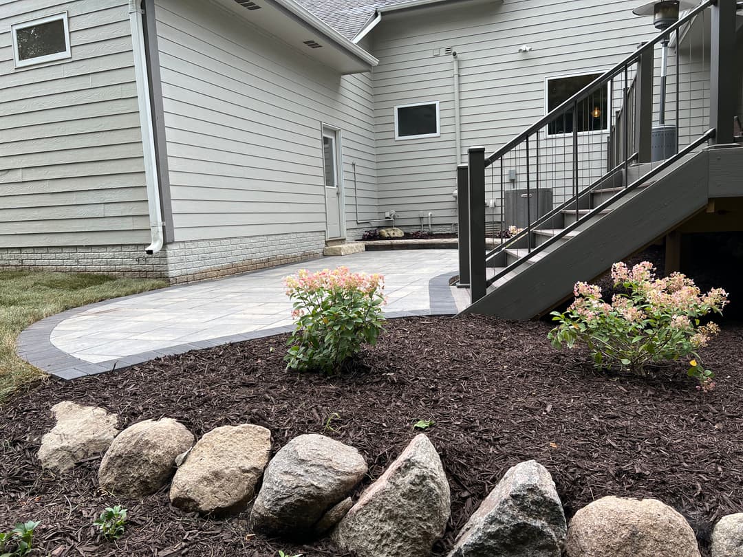 Backyard patio with stone pathway, landscaped flowers, and gray home exterior.