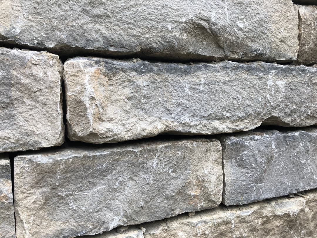 Textured gray stone wall with stacked rectangular stones in natural arrangement.