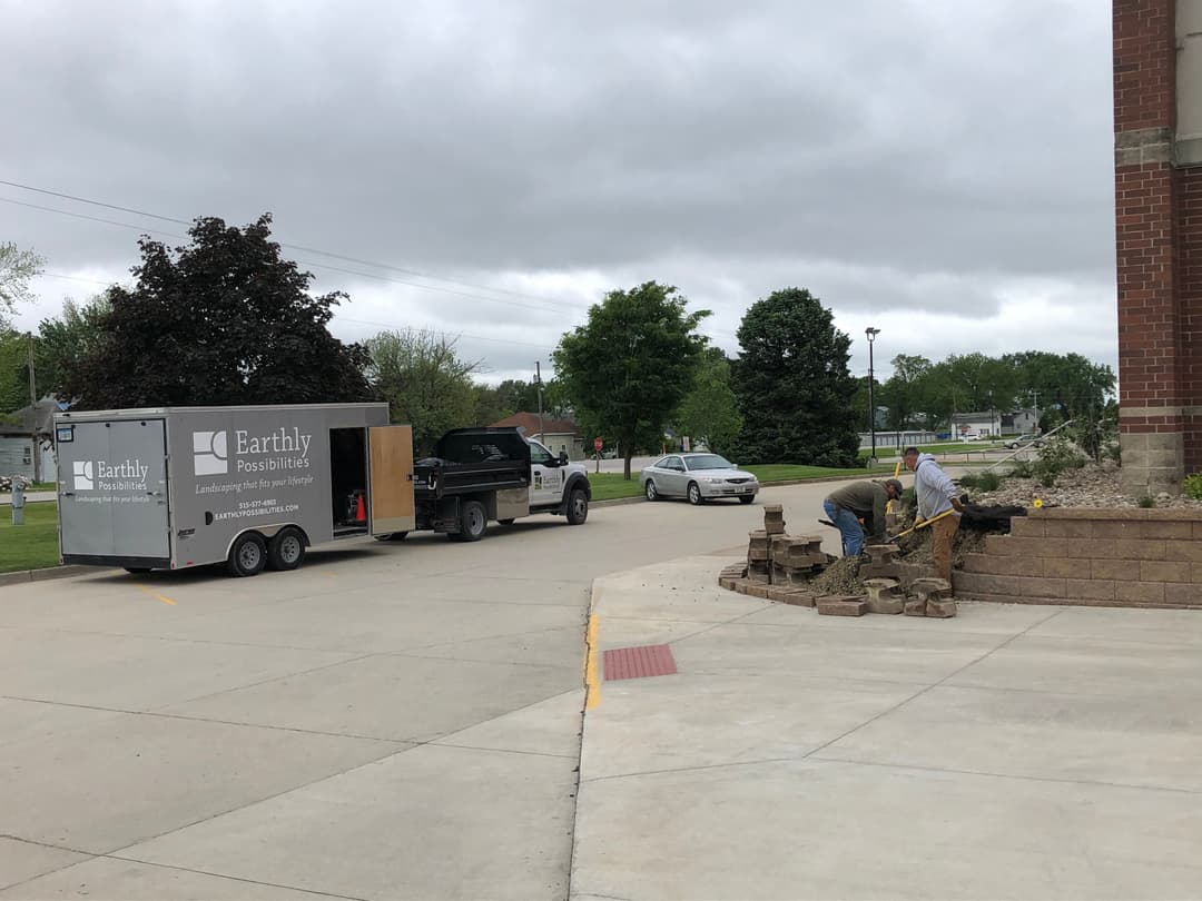 Workers landscaping with stone in front of a truck marked 'Earthly Possibilities.'