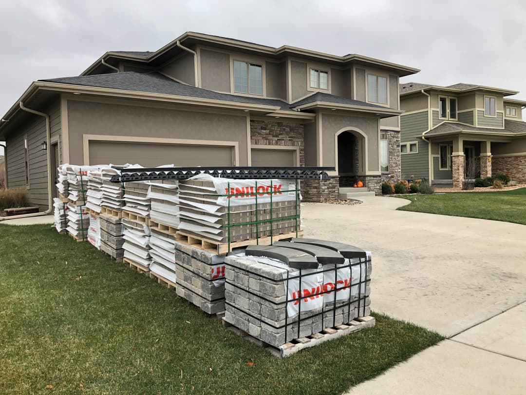 Pallets of construction materials stacked in front of a house under renovation.