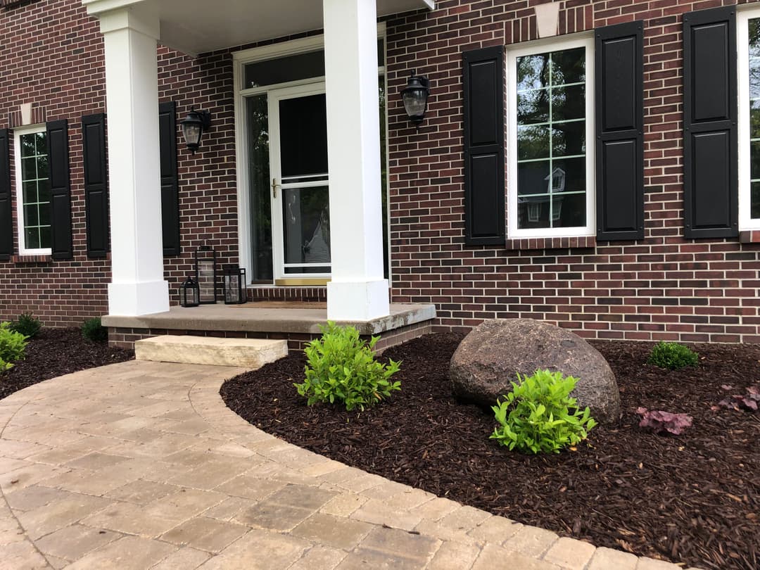 Front porch view with brick siding, landscaping, and a large decorative rock.