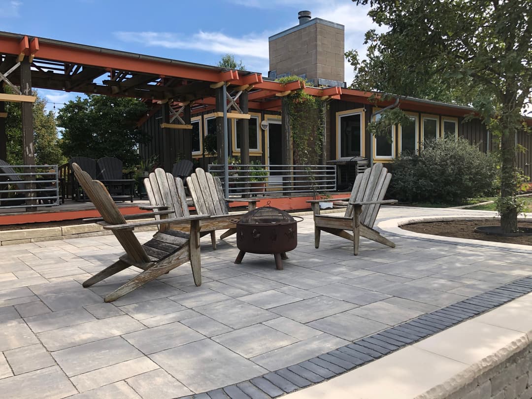 Outdoor patio with wooden Adirondack chairs and a fire pit, surrounded by greenery and a modern home.