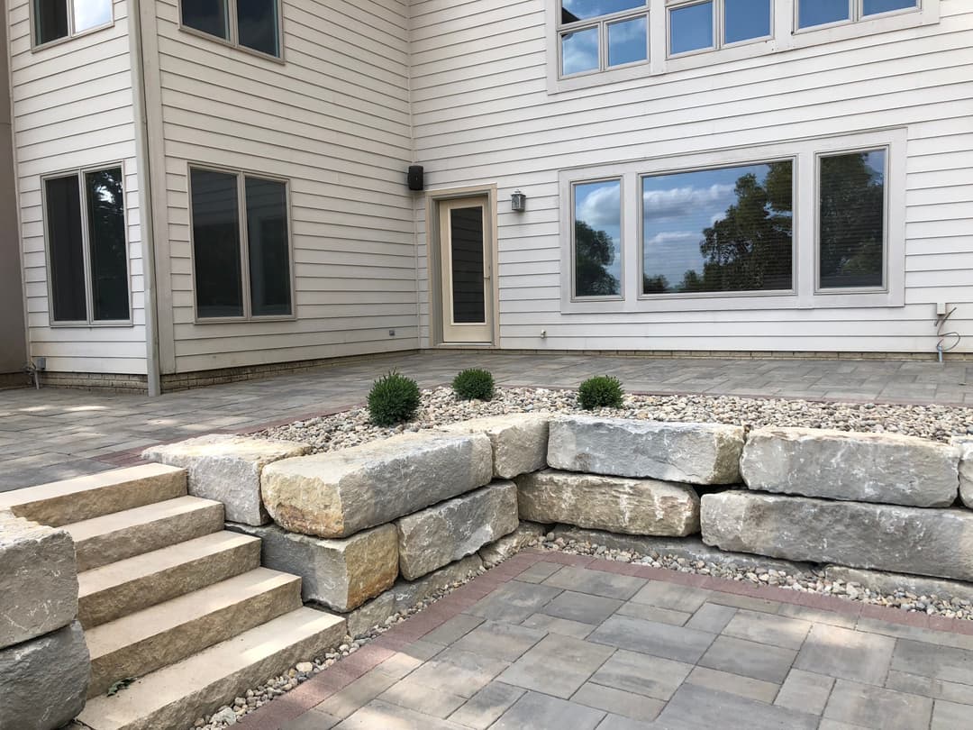 Modern patio area featuring stone steps, natural stone walls, and landscaped greenery.