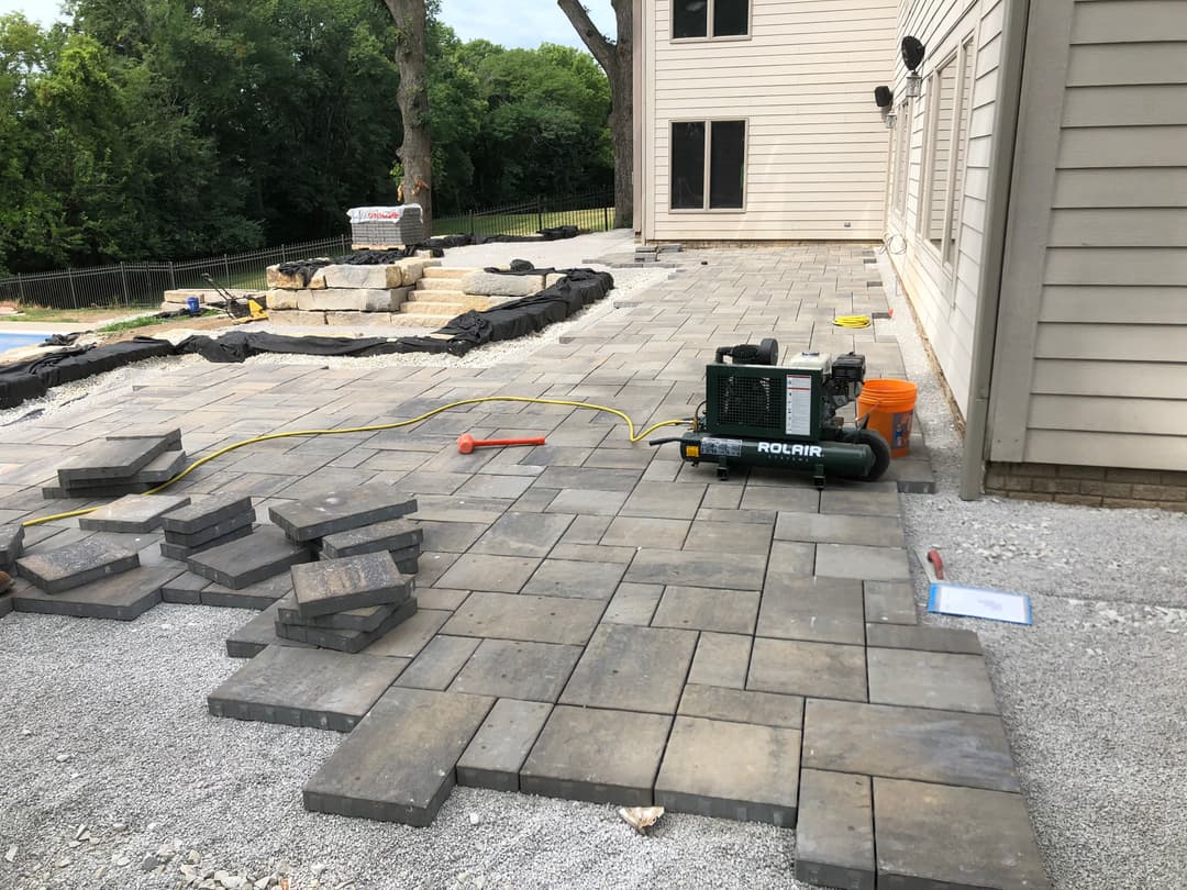 Paved patio installation with stone blocks and construction equipment beside a house.