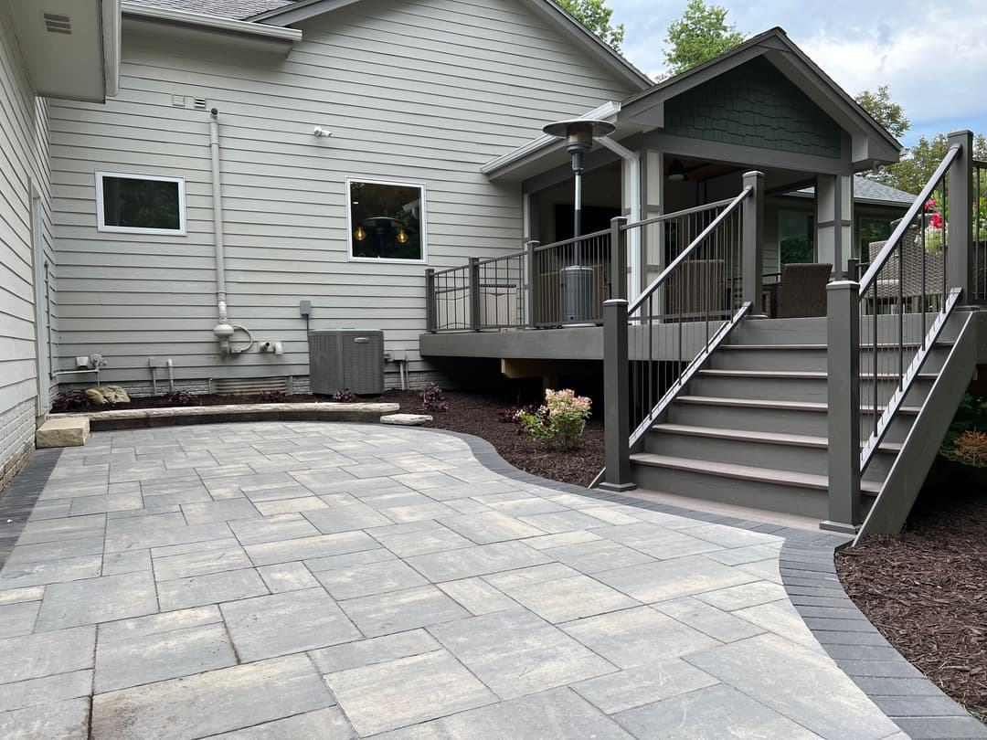 Modern home exterior with paved patio, stairs, railing, and landscaped garden.