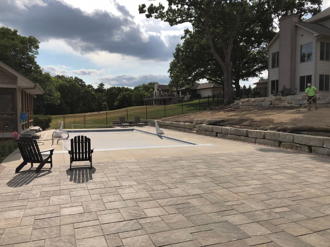 Backyard with an unfinished pool, patio area, and adjacent house under a cloudy sky.