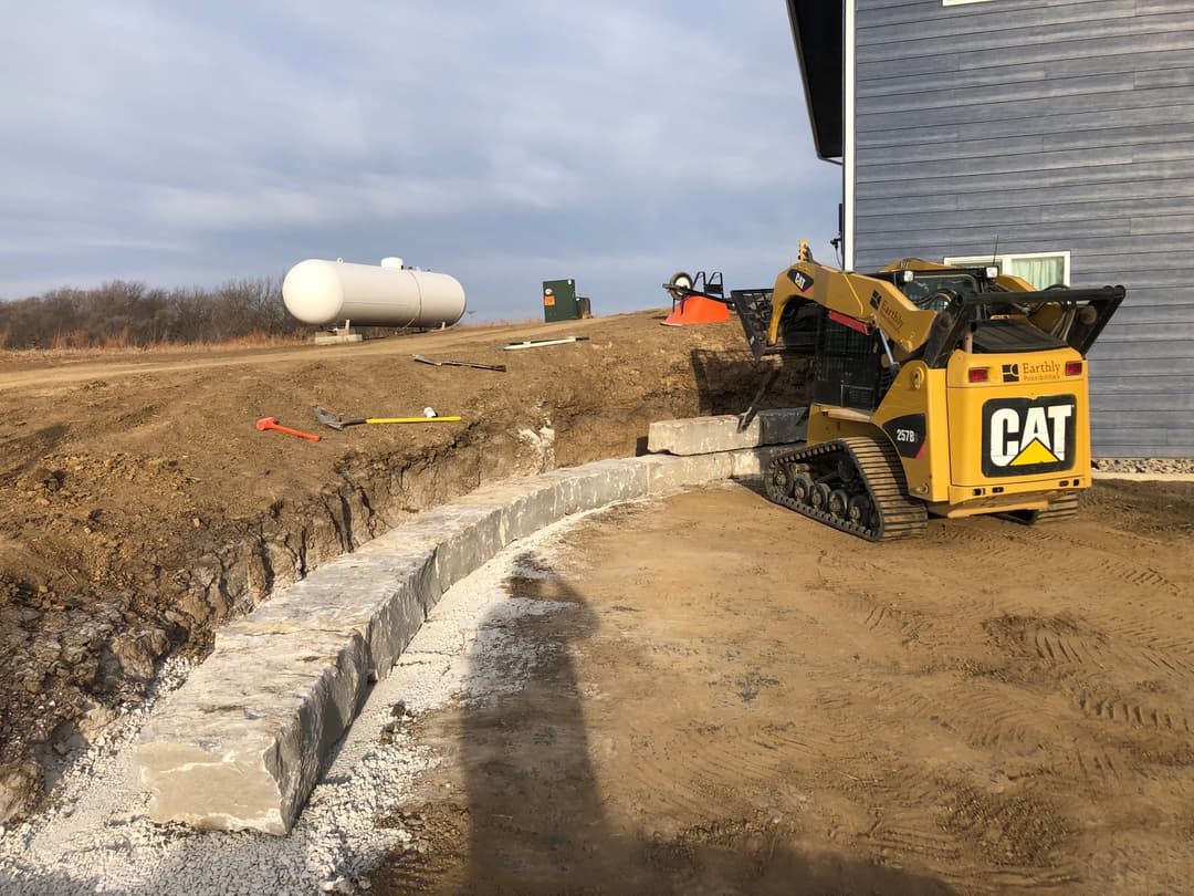 CAT skid steer loader on a construction site with stone wall and equipment in background.