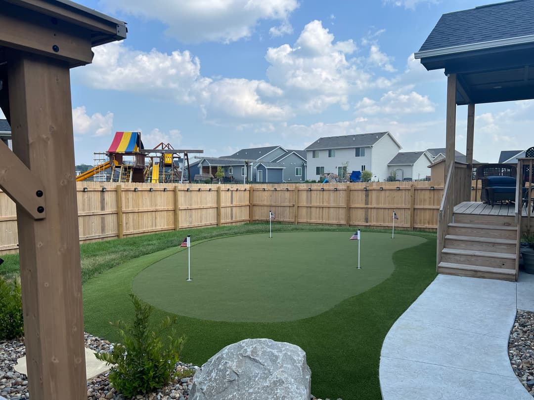 backyard putting green with flags, fenced yard, colorful playground equipment in distance