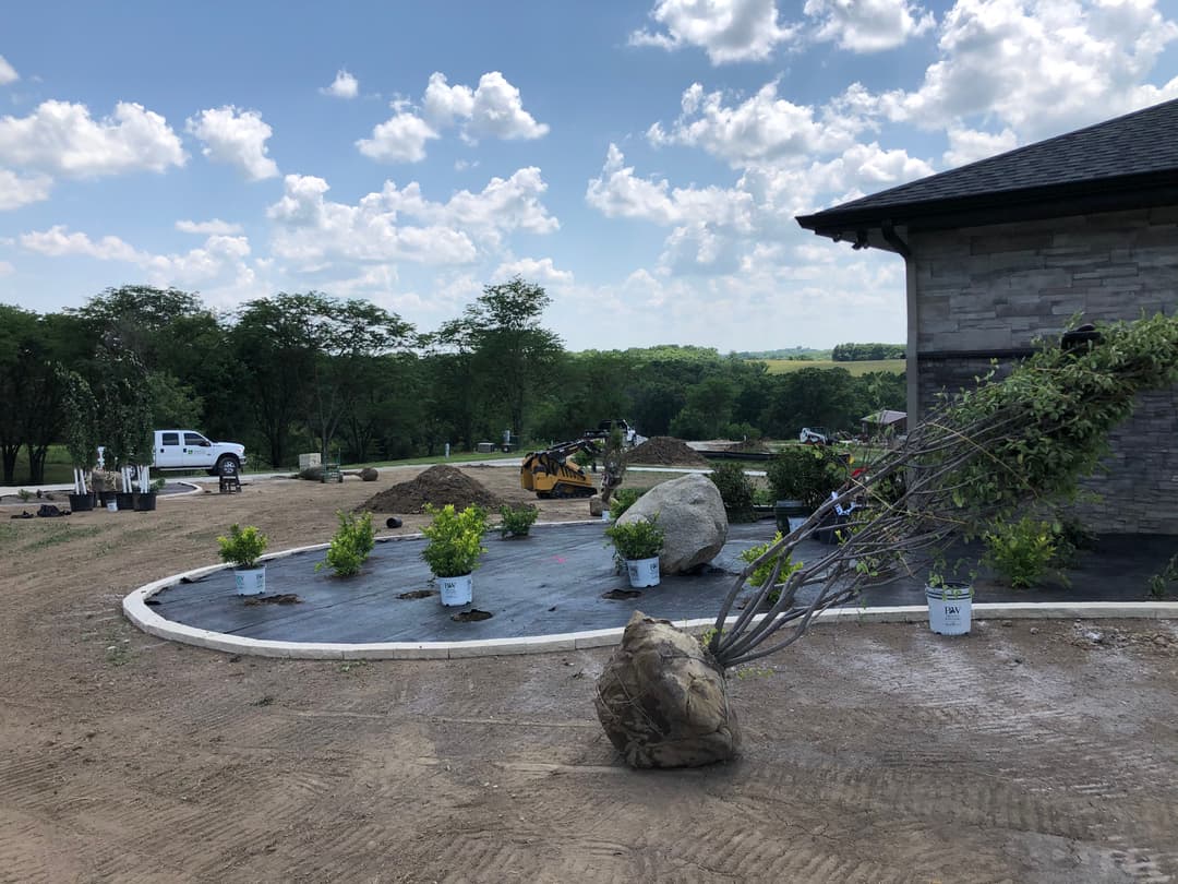 Construction site with new landscaping, featuring plants, rocks, and a work vehicle on a sunny day.