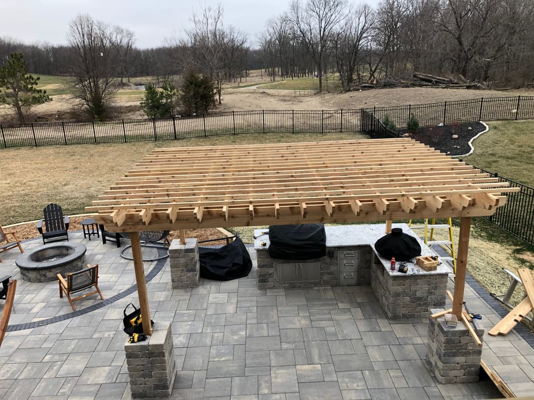 Wooden pergola over outdoor kitchen and fire pit in residential backyard setting.