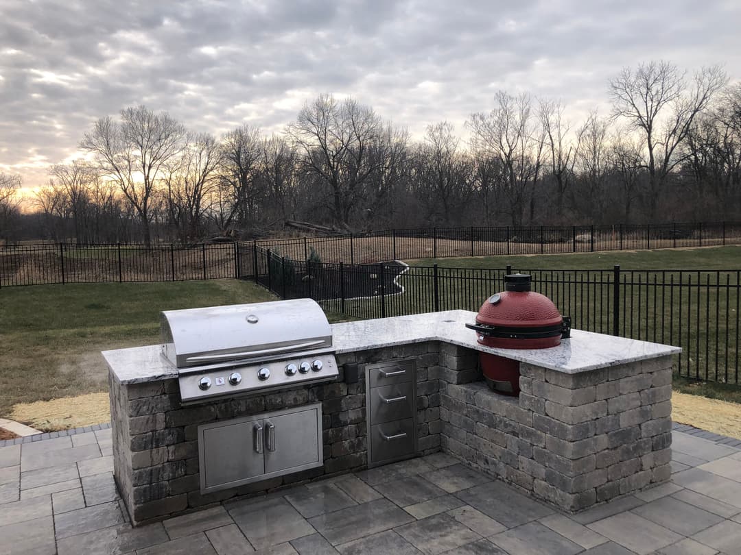 Outdoor kitchen with grill and smoker, stone countertop, and scenic backyard view.