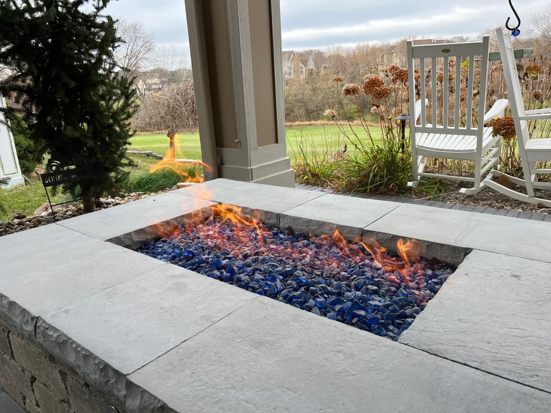 Modern fire pit with blue glass accents and flames, set on a patio with a scenic view.