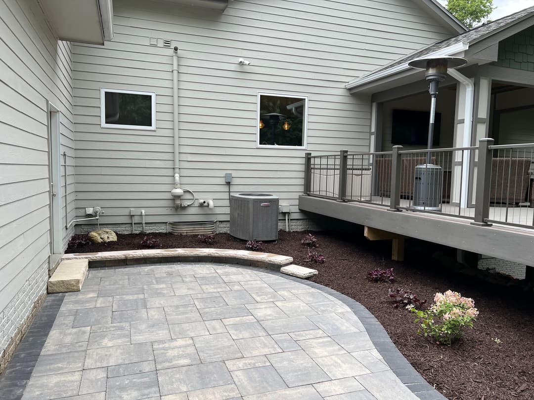 Patio area featuring gray paving stones, landscaping, and modern outdoor heating unit.