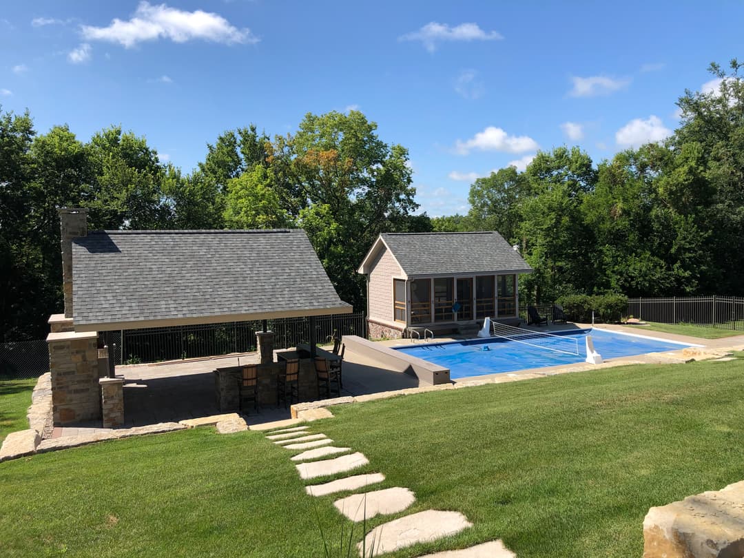 Backyard with pool, stone patio, and two modern gazebos under a clear blue sky.