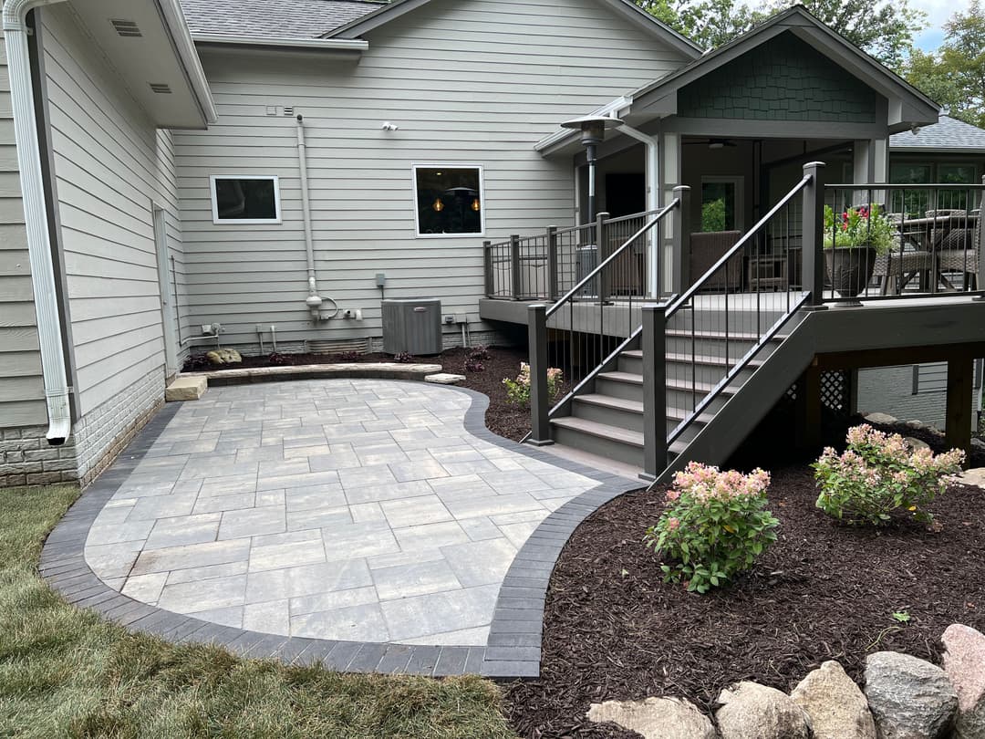 Paved patio leading to a deck with modern railing and landscaped garden in a residential setting.