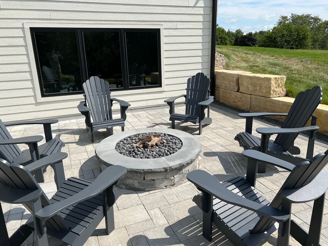 Outdoor patio featuring eight gray Adirondack chairs surrounding a stone fire pit.
