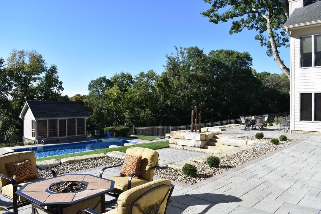 Backyard oasis with a pool, patio seating, and lush landscaping under a clear blue sky.