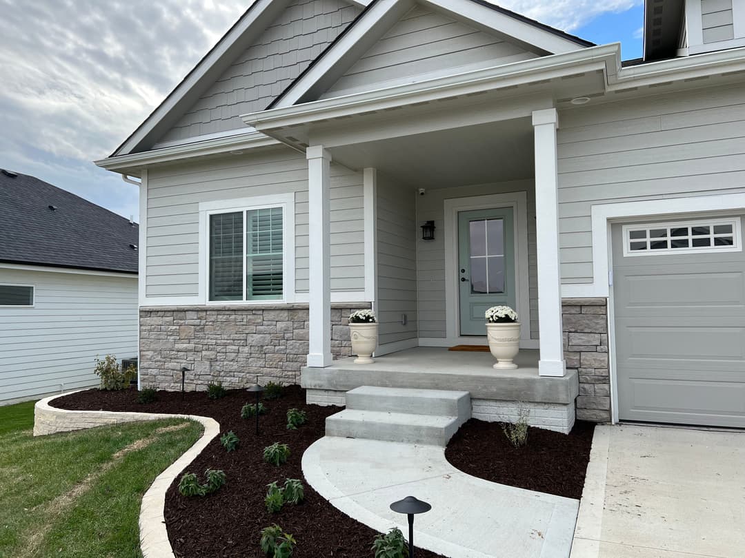 Modern home entrance with stone accents, flower pots, and landscaped pathway.