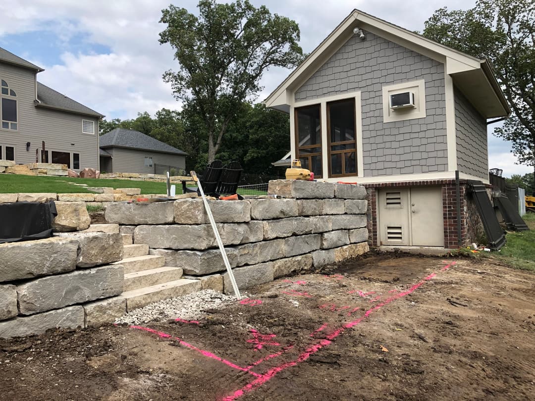 Stone retaining wall and steps leading to a house under construction with landscaping work.
