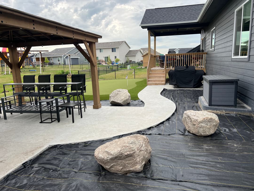 Modern backyard with a gazebo, seating area, pathway, and landscaped rocks.