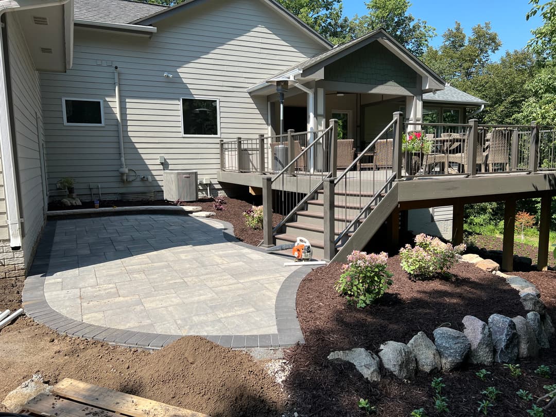 Backyard patio featuring stone pavers, landscaped flower beds, and a spacious deck with railing.
