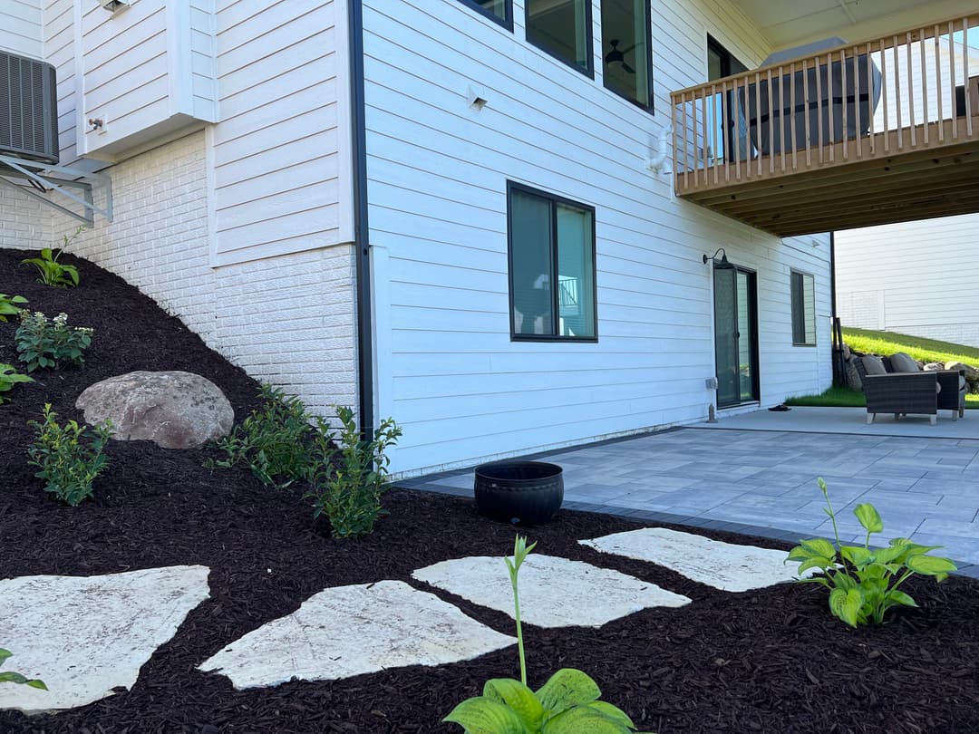 Modern home exterior with landscaped garden, patio stones, and outdoor seating area.