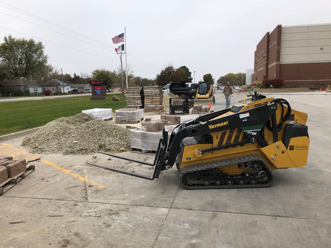 Vermeer mini skid steer loader working at a construction site with pallets of materials.